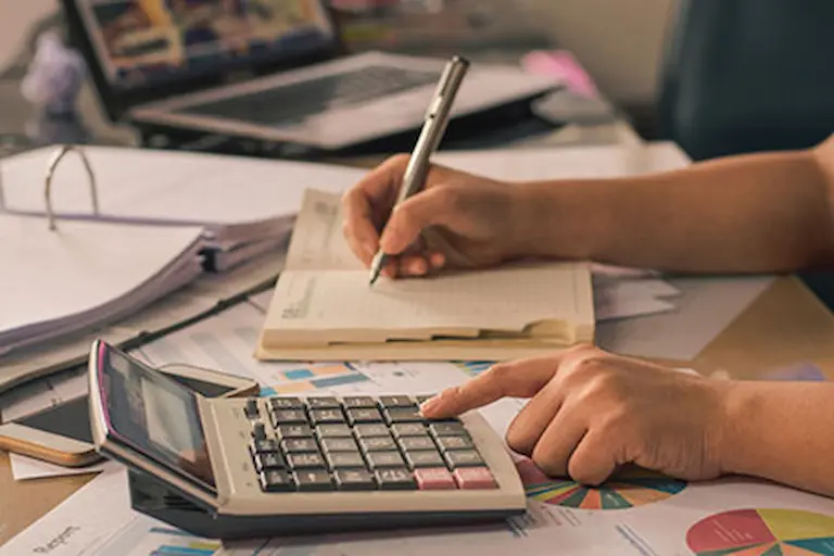 Business owner manually calculating bookkeeping records with a calculator and notebook