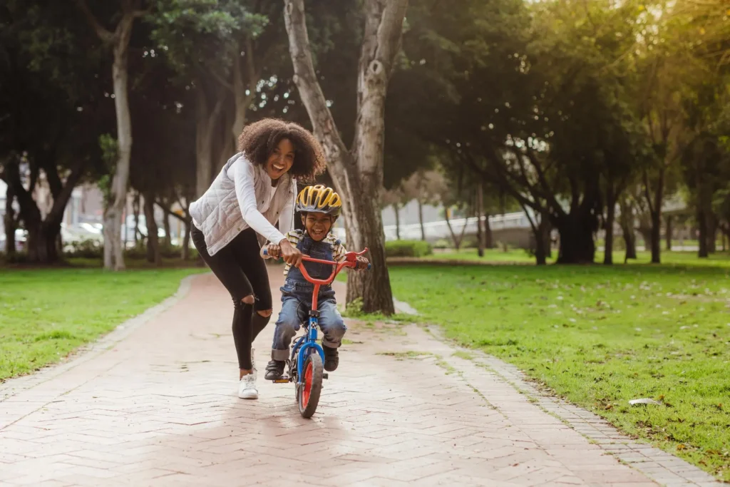 Mother helping her young son ride a bicycle, representing parents saving and investing for their child’s financial future.